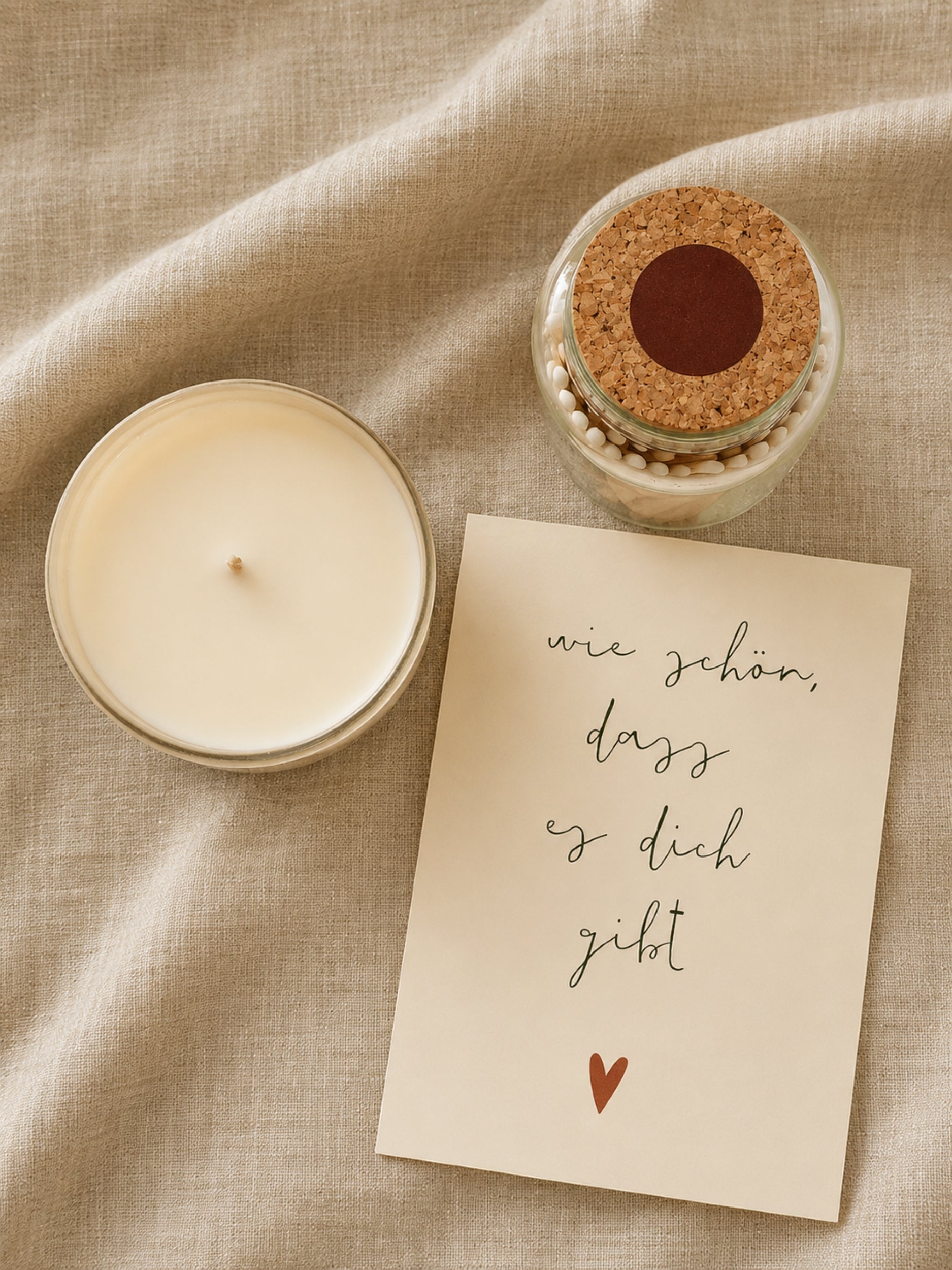 Postkarte "Wie schön, dass es dich gibt" neben Duftkerze und Streichholzglas