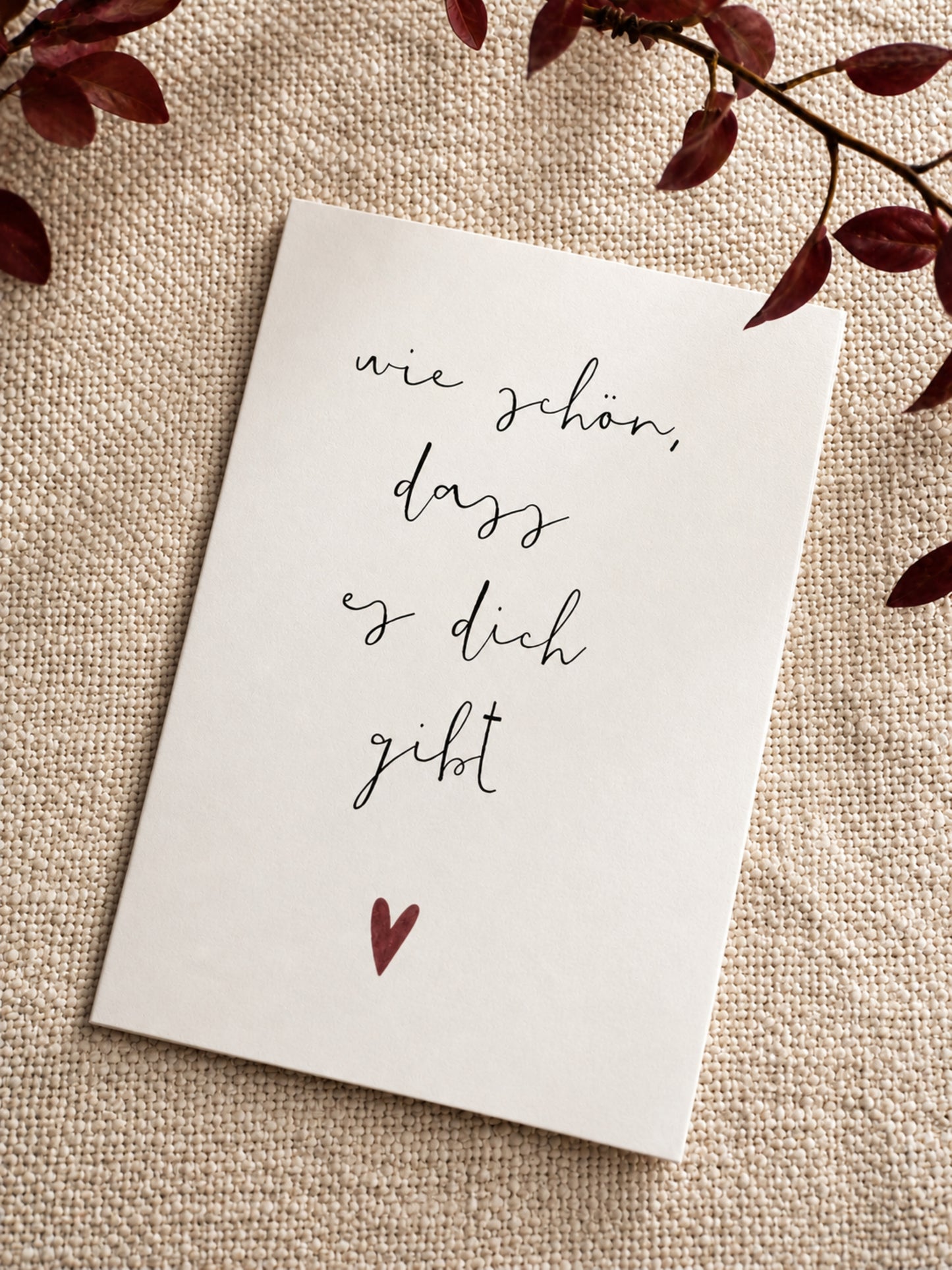 Postkarte "Wie schön, dass es dich gibt" auf naturfarbenem Stoff mit roten Zweigen