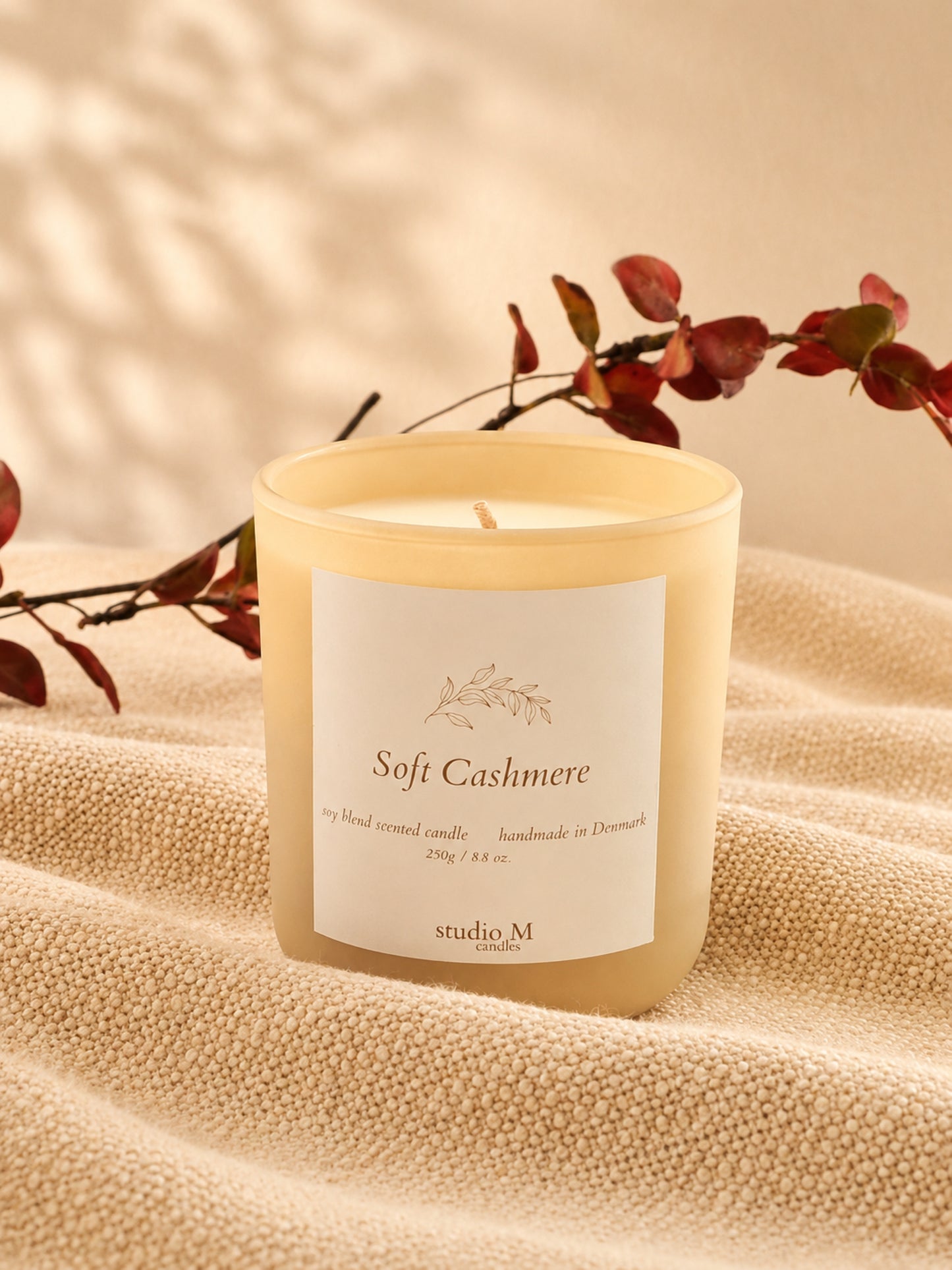 Duftkerze Soft Cashmere auf hellem Stoff mit dekorativen Zweigen