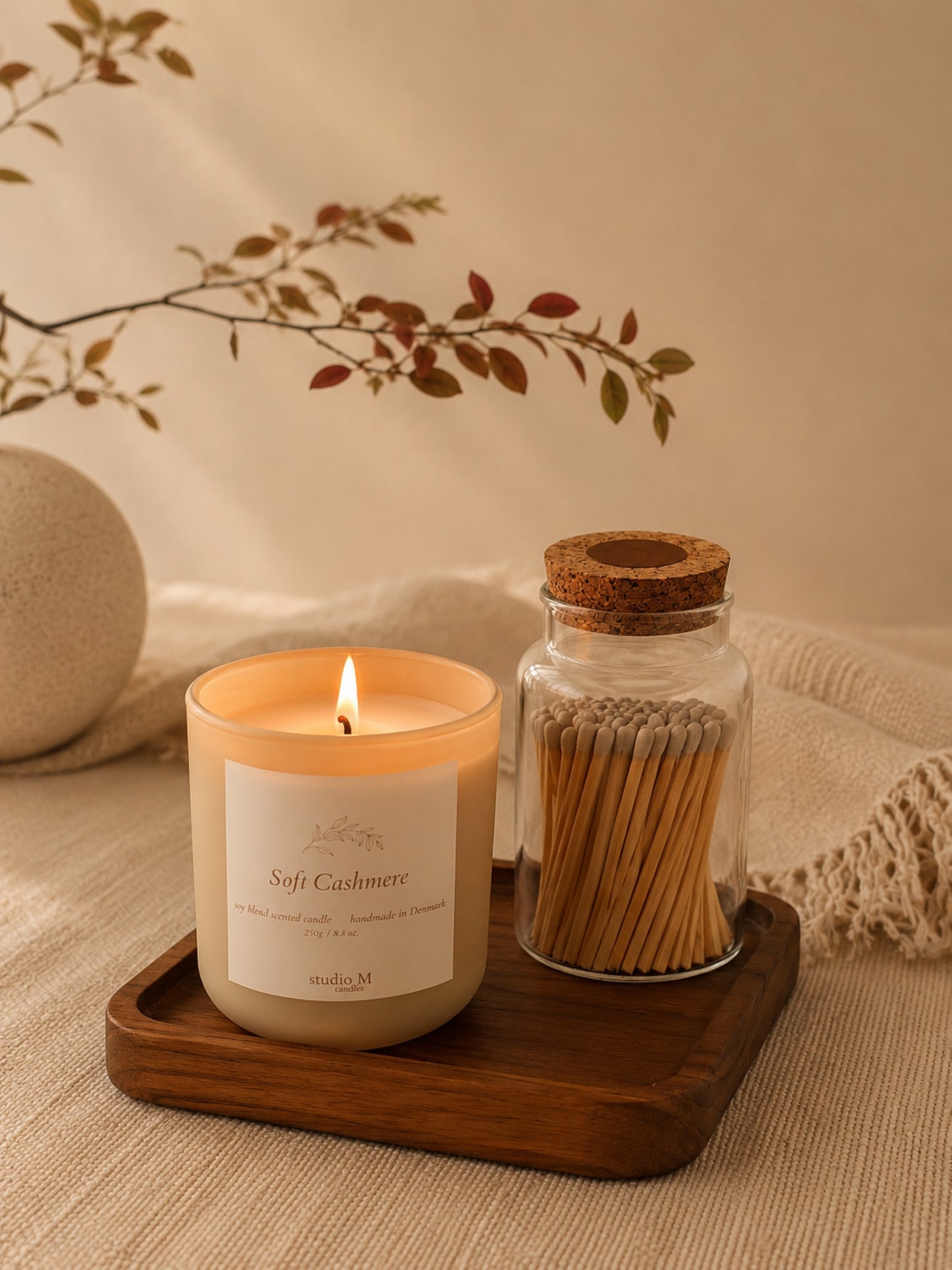 Duftkerze "Soft Cashmere" und Streichholzglas auf Naturholztablett bei Kerzenschein